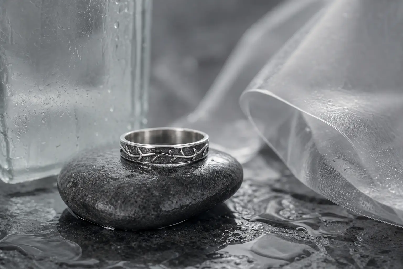 Oxidized silver ring with a vine-like engraved line on wet stone