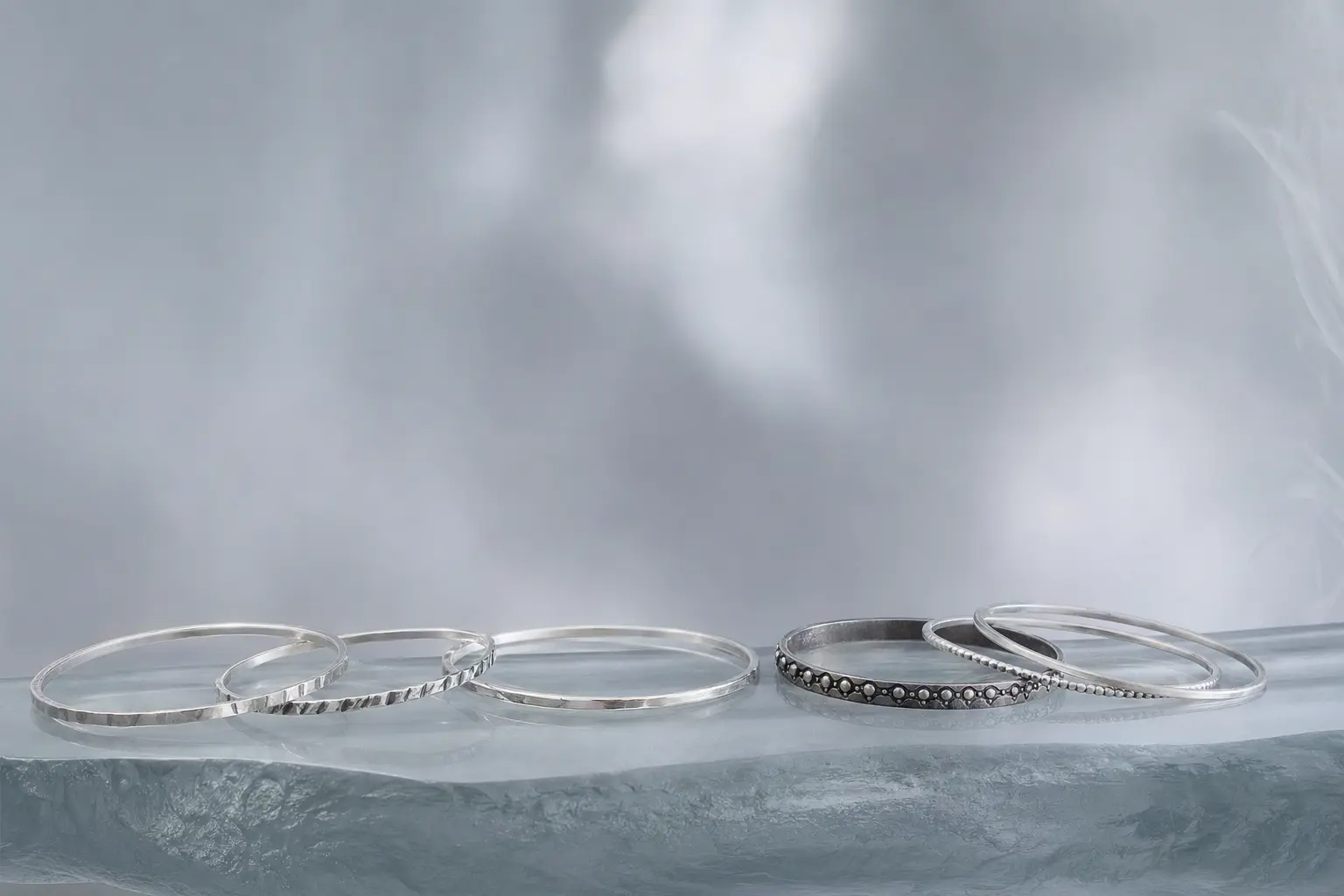 Thin silver bangles loosely spaced along a frosted glass ledge