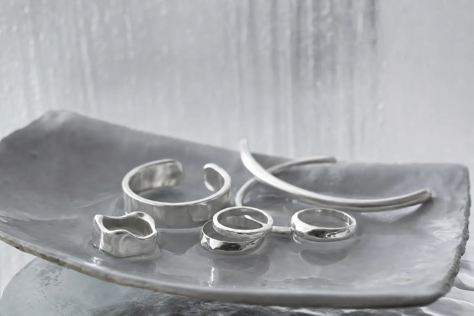 Loose silver rings and bracelet samples on a cool ceramic dish