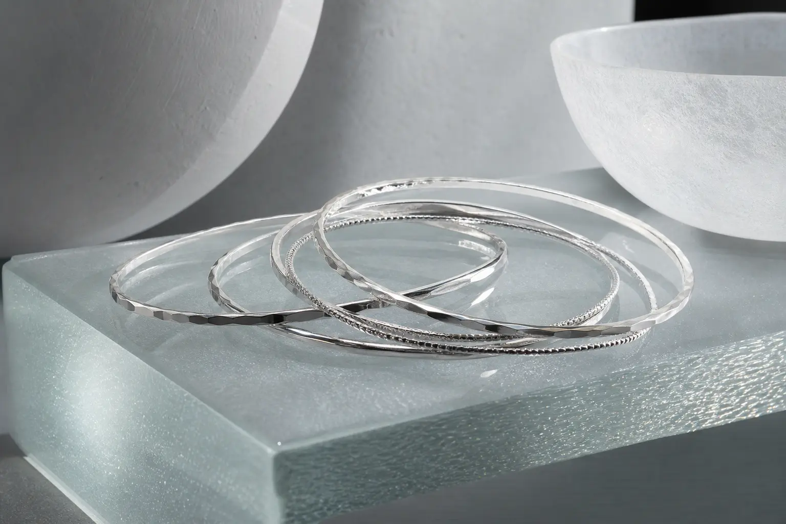 Slim silver bangles overlapping on a frosted glass ledge