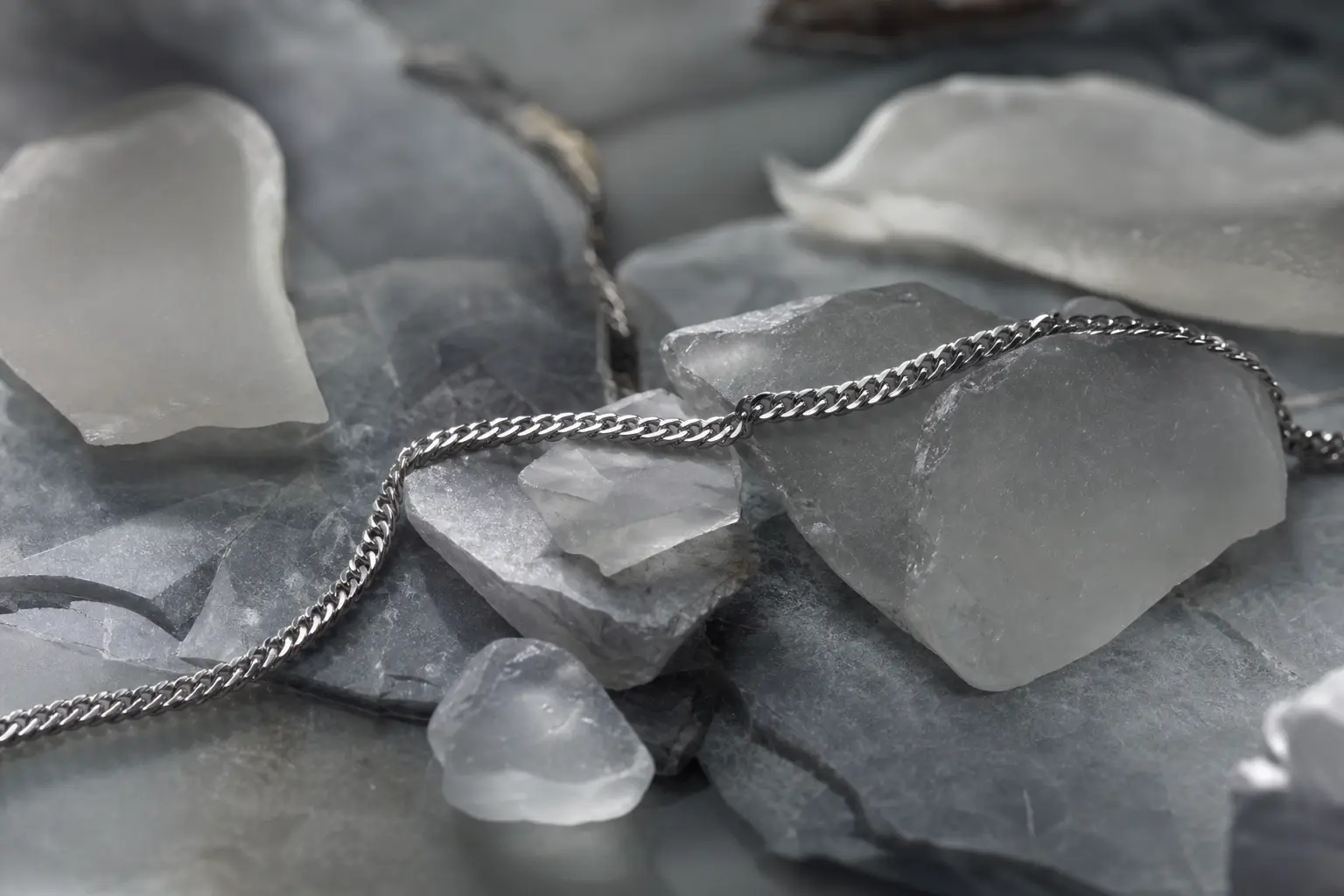 Silver chain crossing smoky sea-glass shards on gray stone